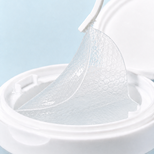 A close-up of a translucent, textured sheet being lifted from a white round container against a soft light blue background.