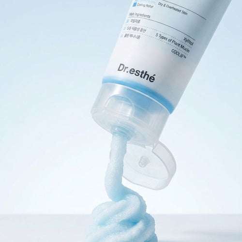 A squeeze tube of Dr. Esthé skincare cream tilted on a white surface, dispensing a thick, light blue cream swirl against a clean white and light blue background.
