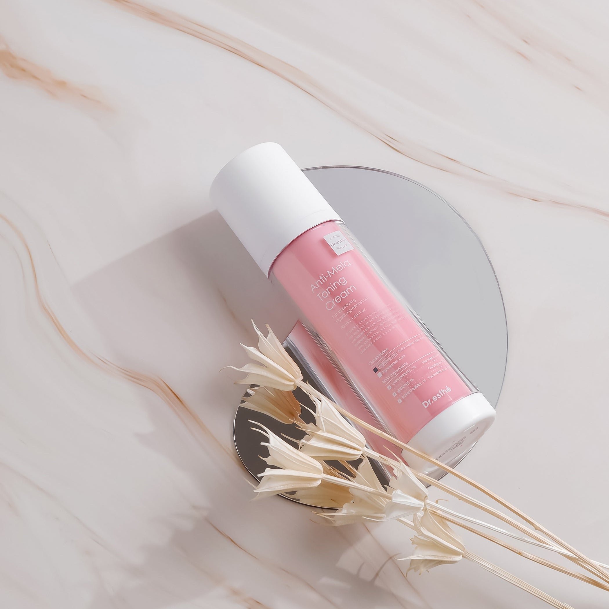 Pink and white Dr. Esthe cosmetic tube on a marble surface with dried flowers