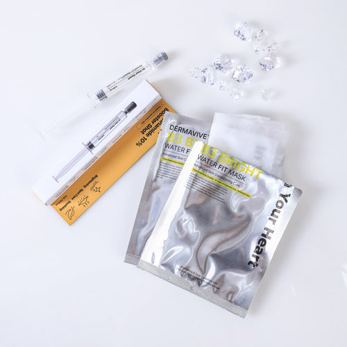 A skincare set laid out on a white background, including a silver foil packet labeled In Your Heart DERMAVIVE 23 Water Fit Mask, a clear syringe-like applicator in a white and gold box, and several small clear gel drops.