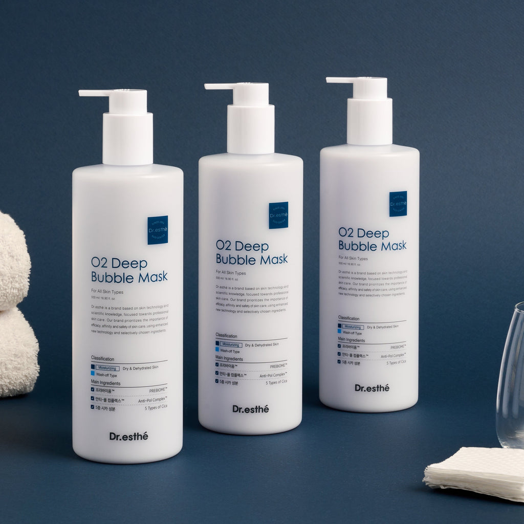 Three bottles of Dr. Esthé O2 Deep Bubble Mask on a dark blue background with towels and a glass.